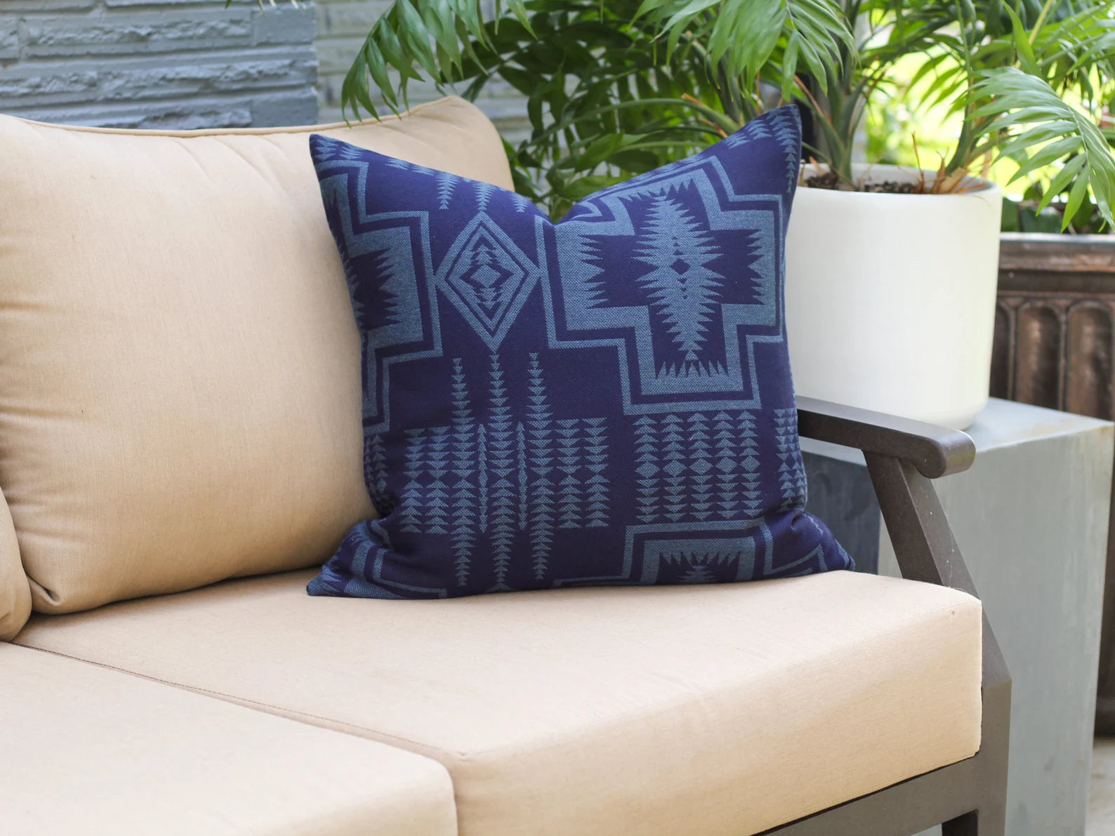 Outdoor pillow the two-tone blue Harding Indigo pattern on a beige outdoor sofa with plants in the background