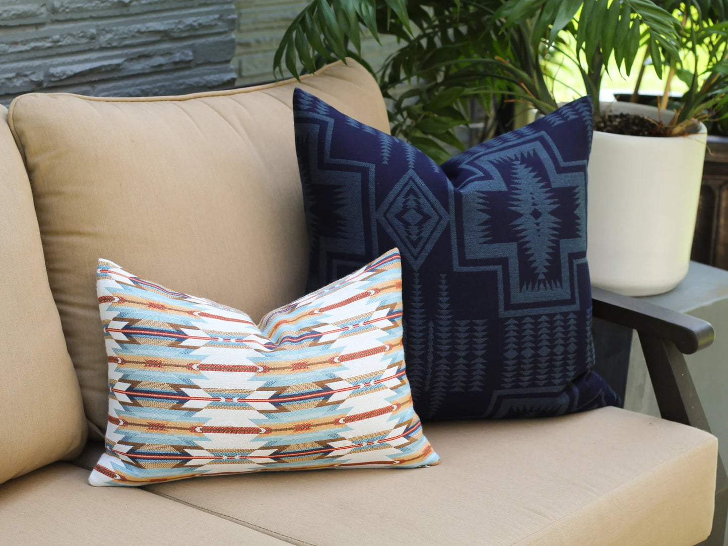 Decorative outdoor pillows on a beige outdoor sofa with plants in the background