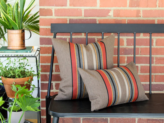 Decorative outdoor pillows in the Yakima Park Umber stripe on a black metal bench against a brick wall.