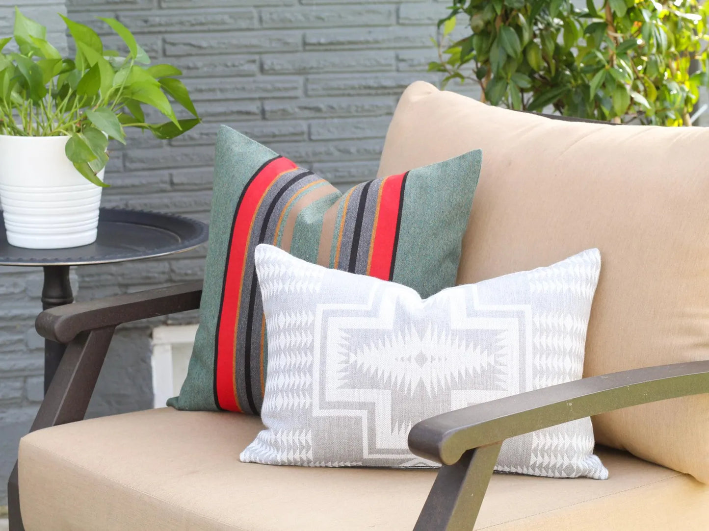 Beige outdoor chair with decorative outdoor pillows and a plant on a table.