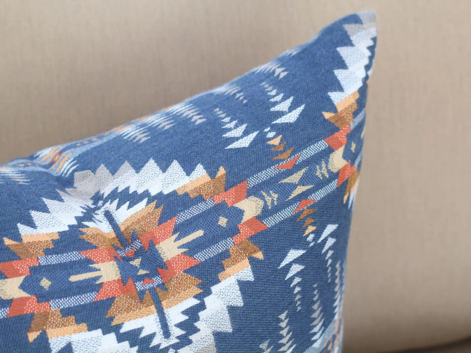 Close up of outdoor pillow in the Juniper Mesa pattern on a beige outdoor sofa. The Juniper Mesa pattern has a dark blue background with shades of brown, orange, yellow, and white in a southwestern pattern.