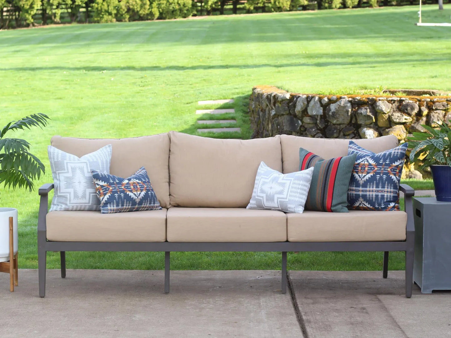 Beige outdoor sofa with patterned cushions on a patio with grass and plants in the background
