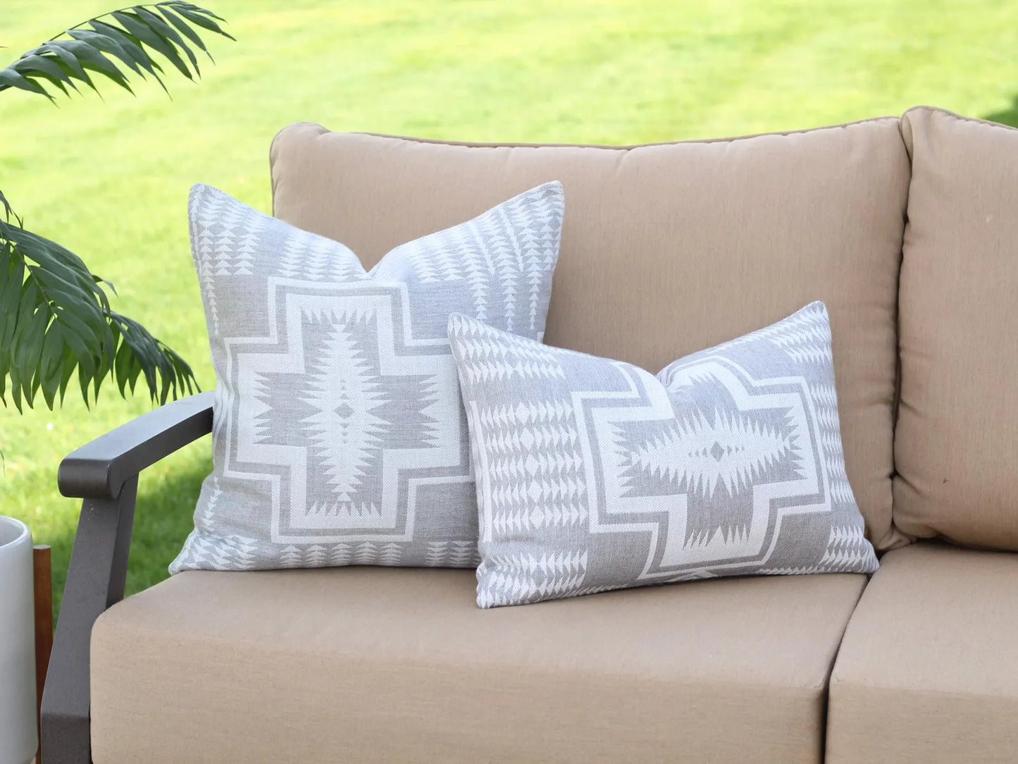 Beige outdoor sofa with two-tone gray outdoor pillows in Harding Dove against a green grass background