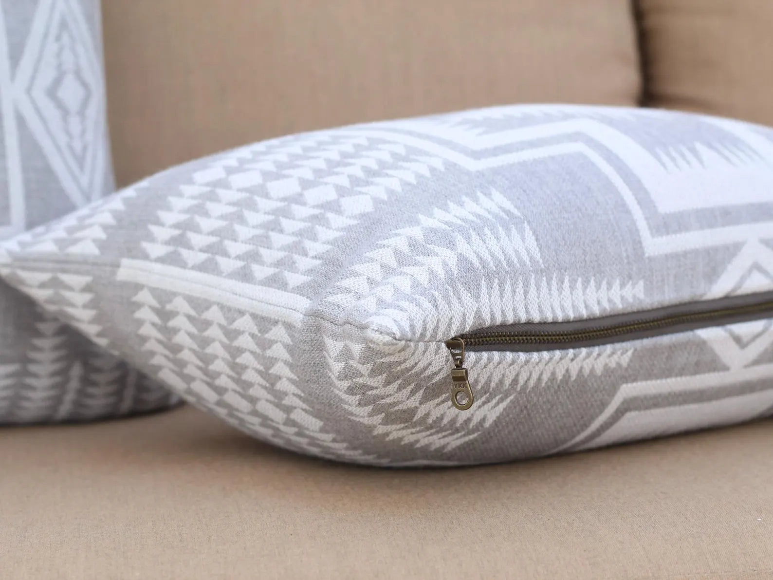 Gray and white patterned pillow with a zipper on a beige couch