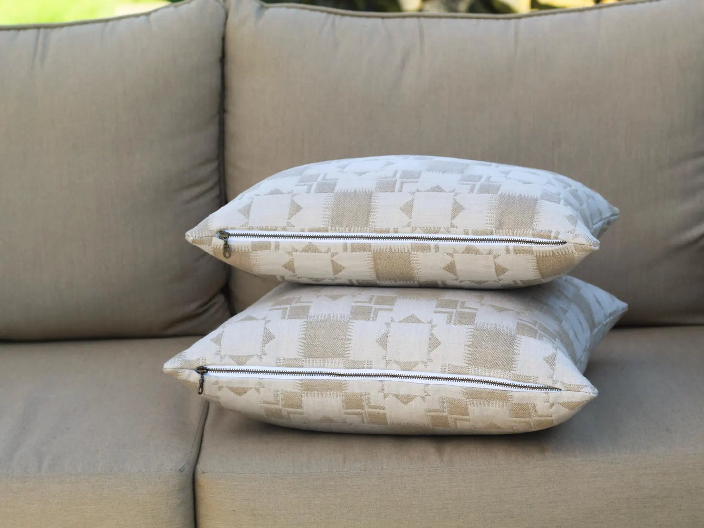 Two outdoor pillows in the Silver Lake Dune pattern stacked on a beige outdoor sofa.