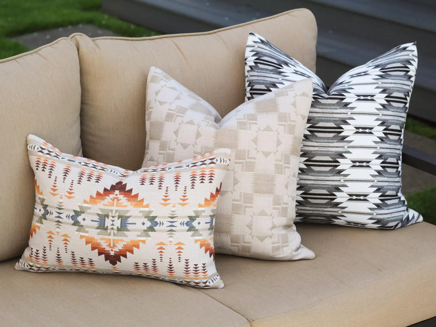 Decorative outdoor pillows with geometric patterns on a beige sofa outdoors.