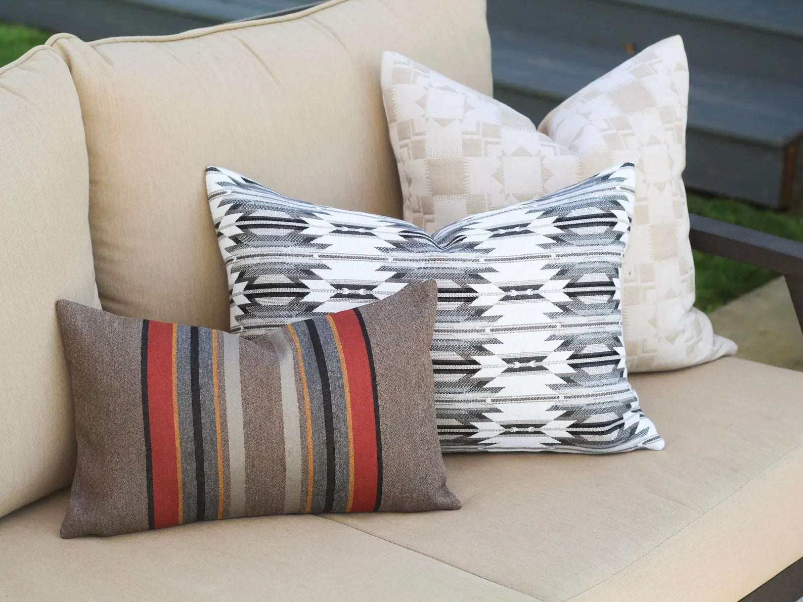 Three outdoor pillows on a beige outdoor sofa with a blurred background