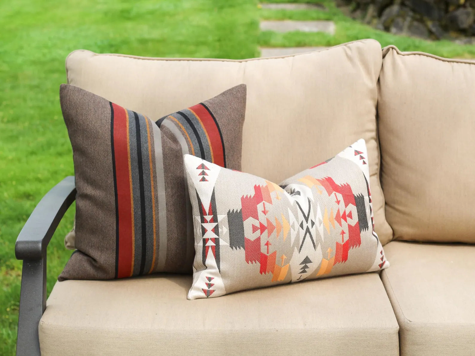 Two decorative pillows on a beige outdoor sofa with a grassy background