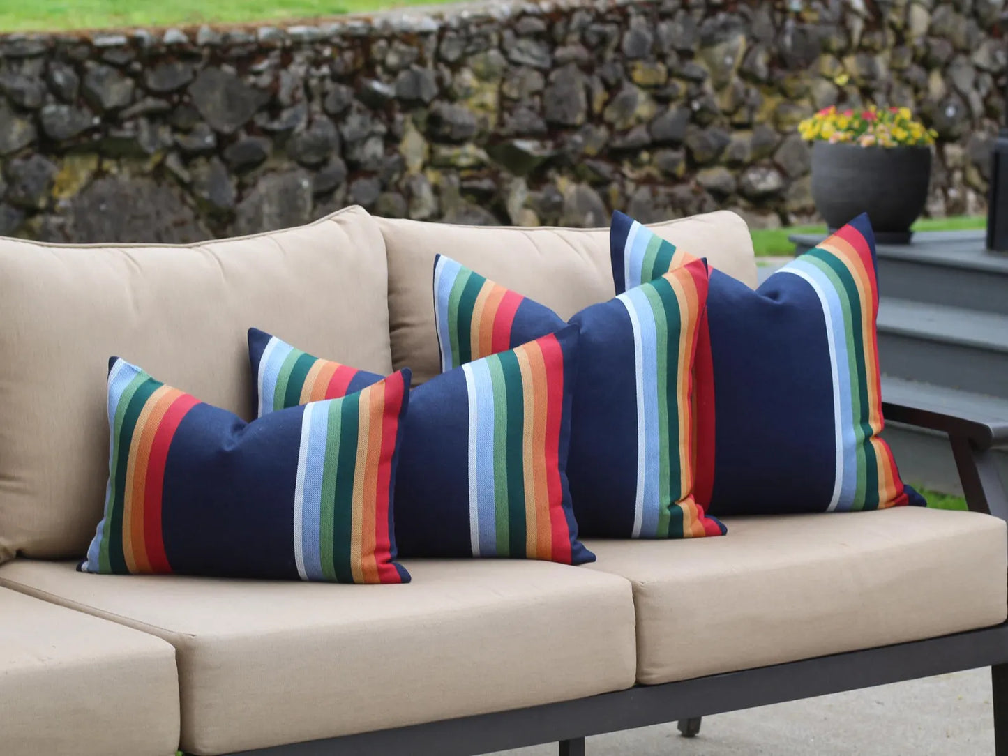 Beige outdoor sofa with colorful striped cushions against a stone wall background