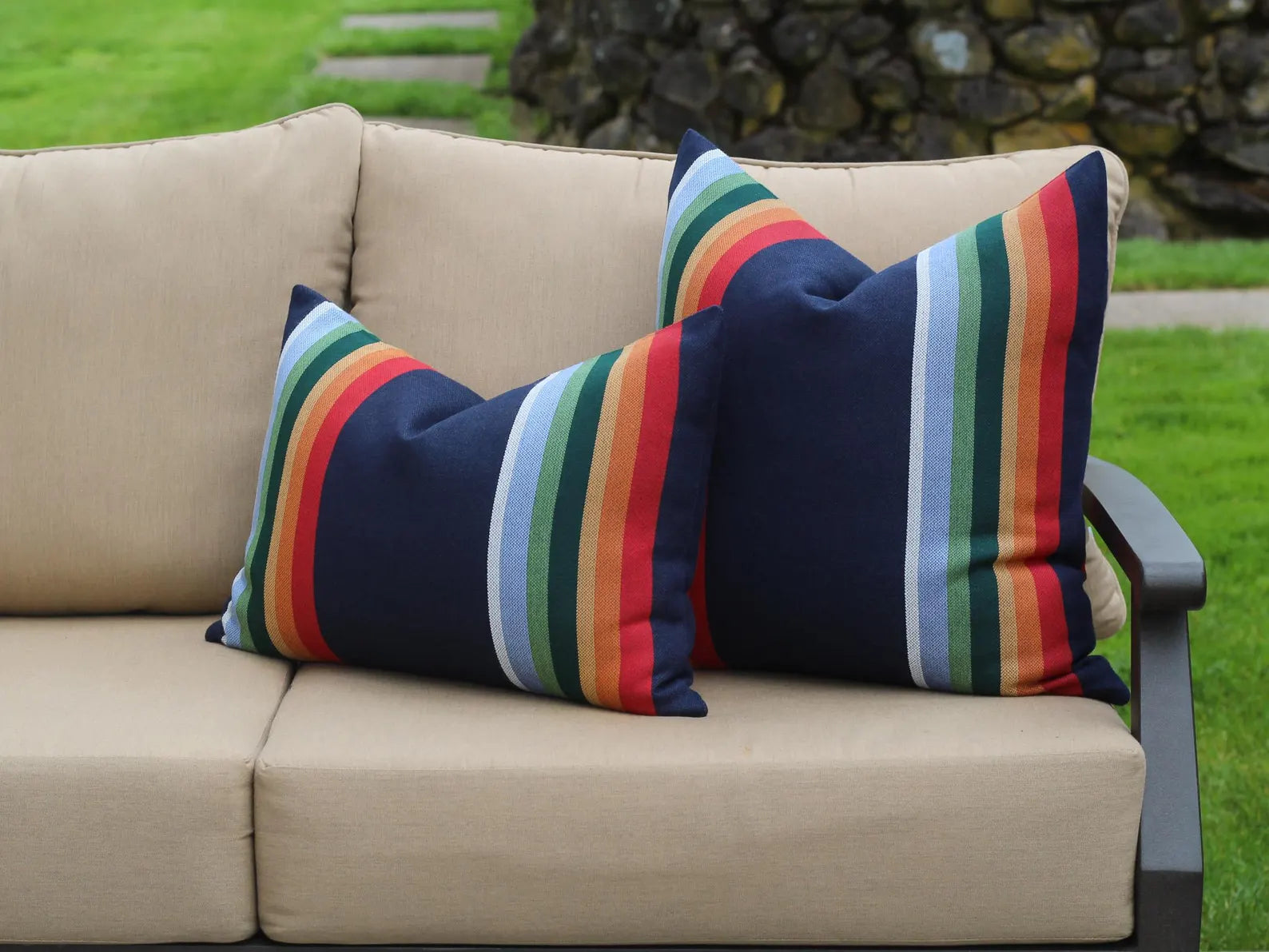 Beige outdoor sofa with colorful striped cushions on a grassy background